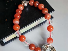 Damenarmband aus rotem Achat Kugeln Bergkristall fein poliert versilberten Details mit chinesischen Schriftzeichen. Flache Ansicht mit einem Buch Damenarmband aus rotem Achat Kugeln Bergkristall fein poliert versilberten Details mit chinesischen Schriftzeichen. Flache Ansicht mit einem Buch