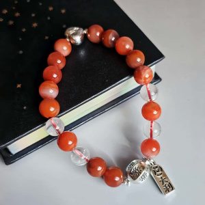 AB-ACT-01-01 Damenarmband aus rotem Achat Kugeln Bergkristall fein poliert versilberten Details mit chinesischen Schriftzeichen. Flache Ansicht mit einem Buch