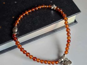 AB-GNA-01-2 Armband Damen mit Granat in Rot Orange Farbton und Fish, Fu Elemente auf ein Buch.