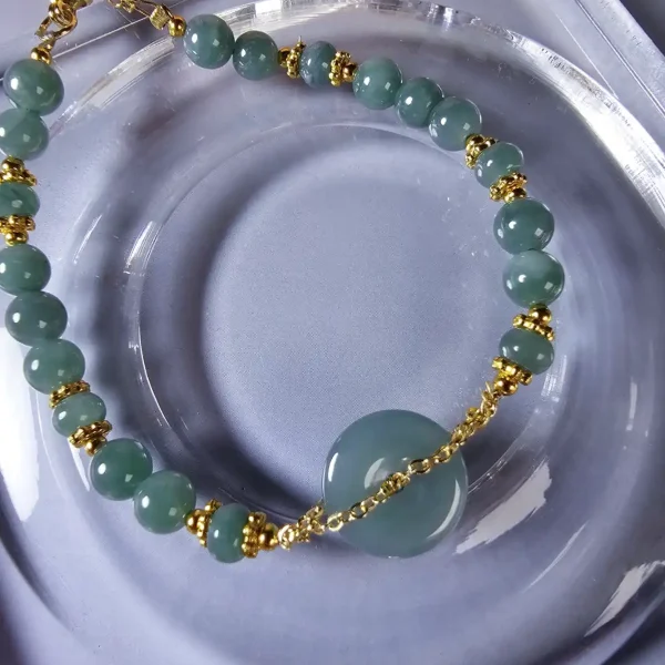 AB-PER-02-06 Handgefertigtes Jade Armband aus blau-grünen Jade-Perlen mit goldenen Trennperlen und einem runden Jade-Anhänger (Ping-An-Knopf). Eleganter Schmuck mit traditioneller chinesischer Symbolik.