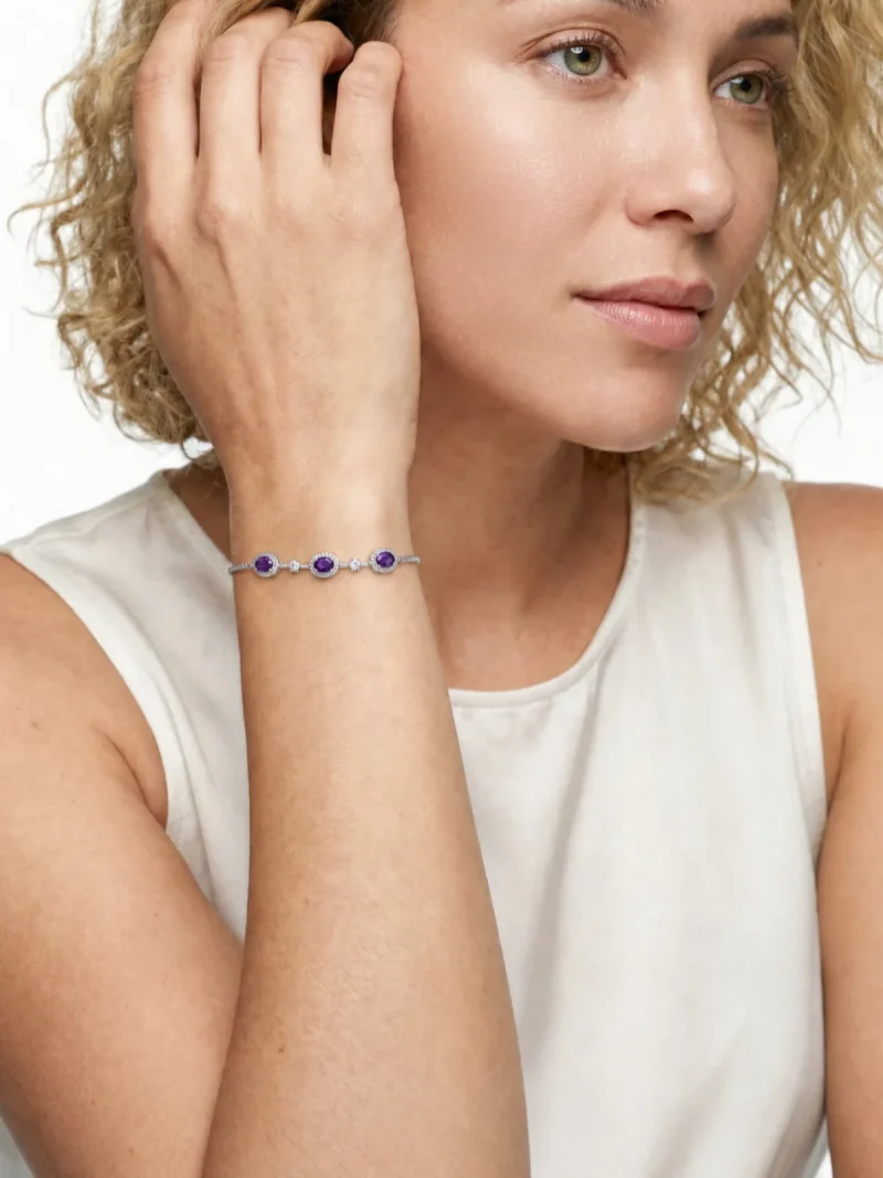 Amethyst Armband aus Kupfer versilbert Nahaufnahme einer Frau in einem hellen ärmellosen Oberteil, die ein filigranes Silberfarbe Armband mit drei violetten Amethyst Edelsteinen und kleinen funkelnden Zirkonia Akzenten am Handgelenk trägt.