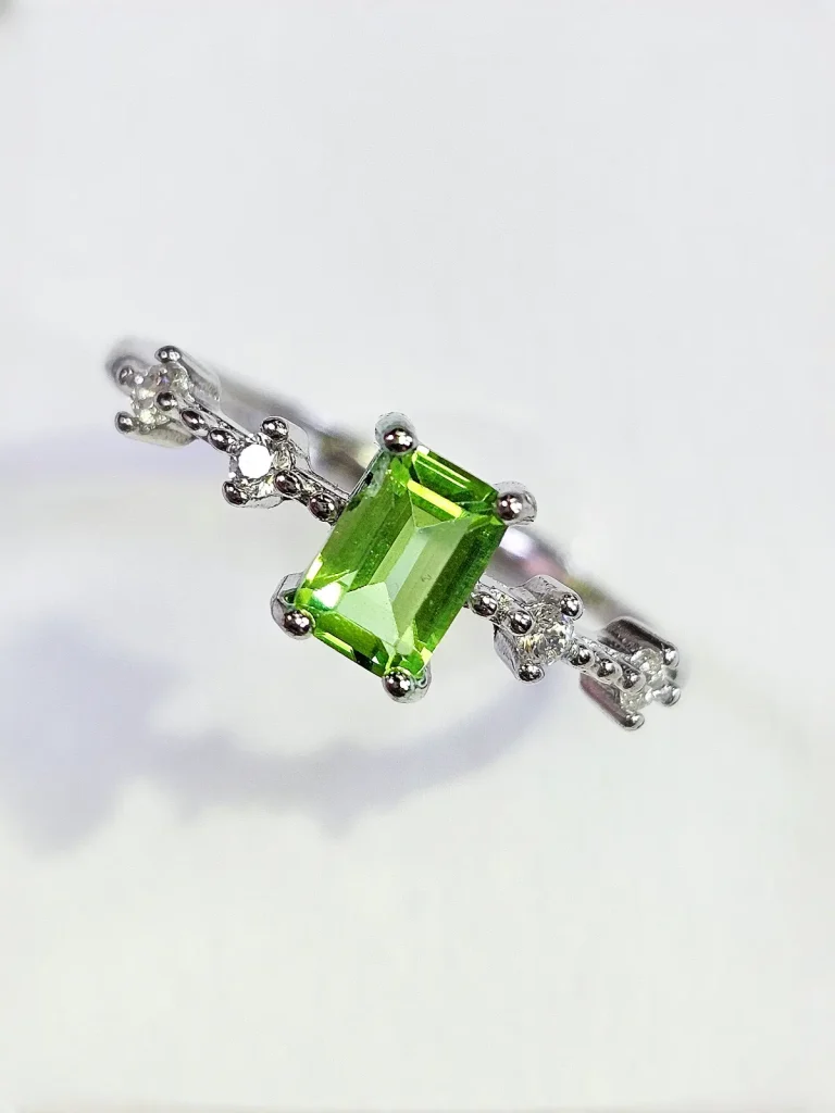 925 Silber Ring mit eckiger Peridot Edelstein – verstellbarer Damenring ein 925er eckiger Peridot-Ring mit grünem Peridot Edelstein und Zirkonia, Geometrisch Look, Smaragdschliff (Emerald Cut), Hauptstein in rechteckiges design, vor ein weißer Hintergrund