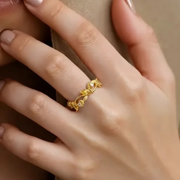 Offener Goldring mit Zirkonia – eleganter Damenring im Vintage Design, Floraler Kranz- Rankenring Eine Hand, die Offener goldfarbener Damenring mit funkelnden Zirkonia Stein präsentiert. Floraler Kranz- Rankenring