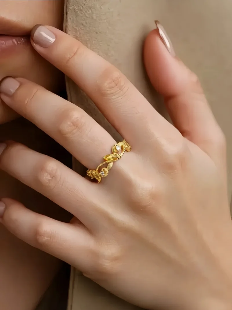 Offener Goldring mit Zirkonia – eleganter Damenring im Vintage Design, Floraler Kranz- Rankenring Eine Hand, die Offener goldfarbener Damenring mit funkelnden Zirkonia Stein präsentiert. Floraler Kranz- Rankenring