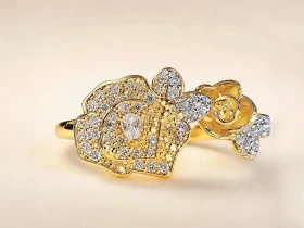 Nahaufnahme einer goldfarbenen Damenring. Der Set zeigt zwei stilisierte Rosenblüten: Eine Blüte ist glatt und poliert, die andere ist dicht mit kleinen, funkelnden Kristallen (Pavé-Optik) besetzt und hat einen größeren Kristall in der Mitte.