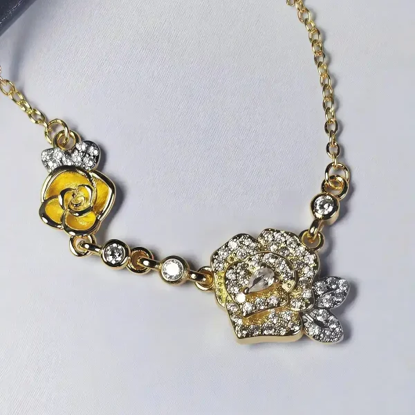 HK-TDG-04-09 Nahaufnahme einer goldfarbenen Halskette aus Kupfer. Der Anhänger zeigt zwei stilisierte Rosenblüten: Eine Blüte ist glatt und poliert, die andere ist dicht mit kleinen, funkelnden Kristallen (Pavé-Optik) besetzt und hat einen größeren Kristall in der Mitte. Die Kette verbindet die Elemente mit kleinen, runden Kristallsteinen.