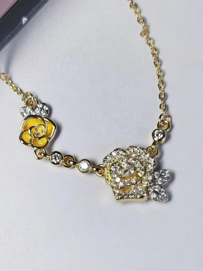 HK-TDG-04-09 Nahaufnahme einer goldfarbenen Halskette aus Kupfer. Der Anhänger zeigt zwei stilisierte Rosenblüten: Eine Blüte ist glatt und poliert, die andere ist dicht mit kleinen, funkelnden Kristallen (Pavé-Optik) besetzt und hat einen größeren Kristall in der Mitte. Die Kette verbindet die Elemente mit kleinen, runden Kristallsteinen.