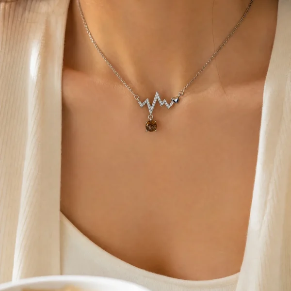 Lifestyle-Aufnahme einer S925 Sterling Silber Halskette mit geometrischem Zickzack-Design, funkelnden Zirkonia, kleinem Herzdetail und braunem Rutilquarz-Anhänger, getragen zu einem eleganten cremefarbenen Outfit.