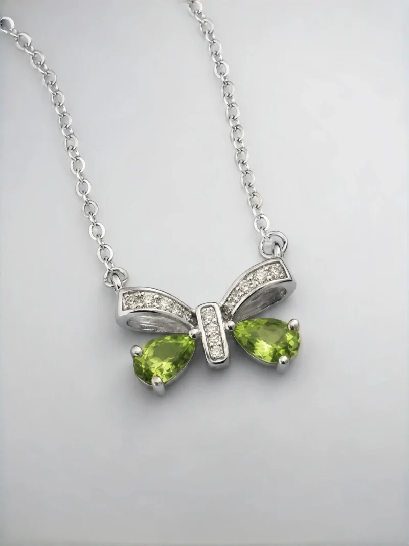 Schleife-HK05-01 ein 925er Silber Halskette mit grünem Peridot Edelstein Anhänger- Schmetterling, vor einer lichtblauer Hintergrund.