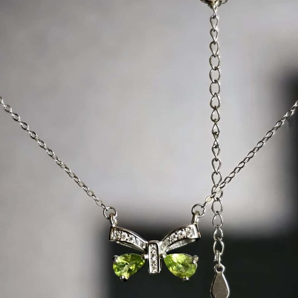 Schleife-HK05-03 ein 925er Silber Halskette mit grünem Peridot Edelstein Anhänger- Schmetterling, vor einer lichtblauer Hintergrund.