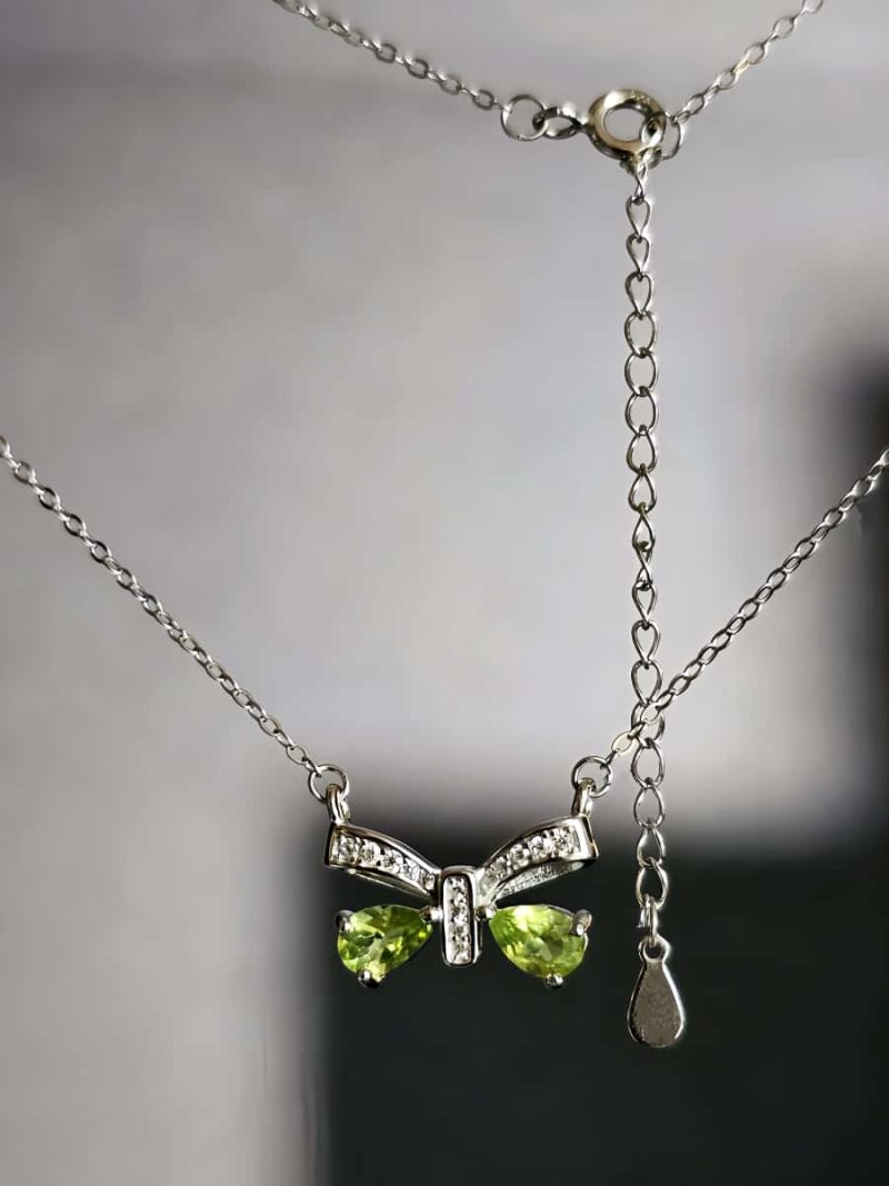 Schleife-HK05-03 ein 925er Silber Halskette mit grünem Peridot Edelstein Anhänger- Schmetterling, vor einer lichtblauer Hintergrund.