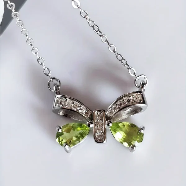 Schleife-HK05-04 ein 925er Silber Halskette mit grünem Peridot Edelstein Anhänger- Schmetterling, vor einer lichtblauer Hintergrund.
