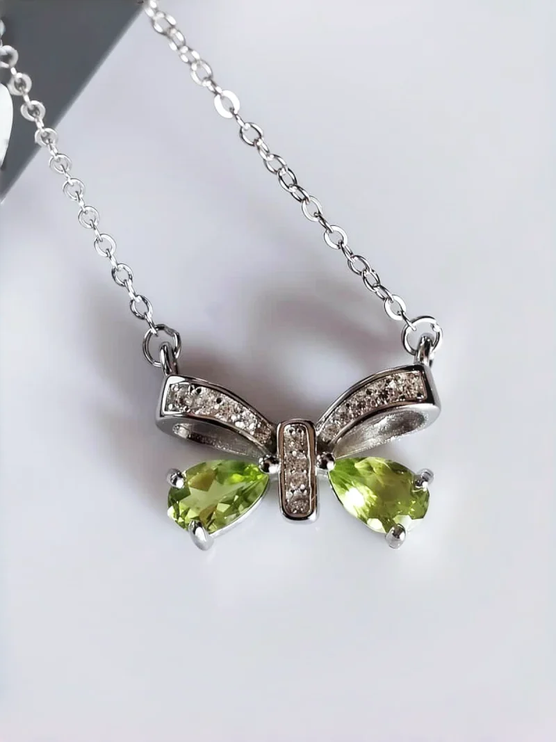 Schleife-HK05-04 ein 925er Silber Halskette mit grünem Peridot Edelstein Anhänger- Schmetterling, vor einer lichtblauer Hintergrund.