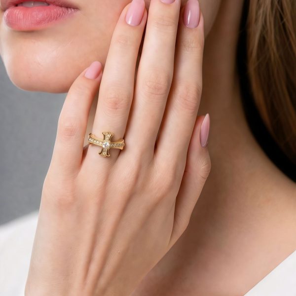 Moderner offener Damenring mit Kreuz-Design Nahaufnahme einer Frauenhand mit einem goldenen Kreuzring, der mit kleinen Zirkonia-Steinen besetzt ist. Der Ring wird elegant am Kinn präsentiert.
