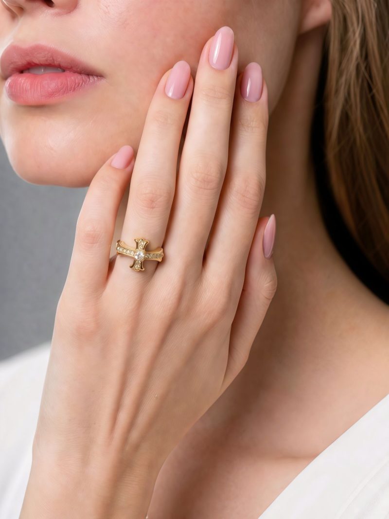 Moderner offener Damenring mit Kreuz-Design Nahaufnahme einer Frauenhand mit einem goldenen Kreuzring, der mit kleinen Zirkonia-Steinen besetzt ist. Der Ring wird elegant am Kinn präsentiert.