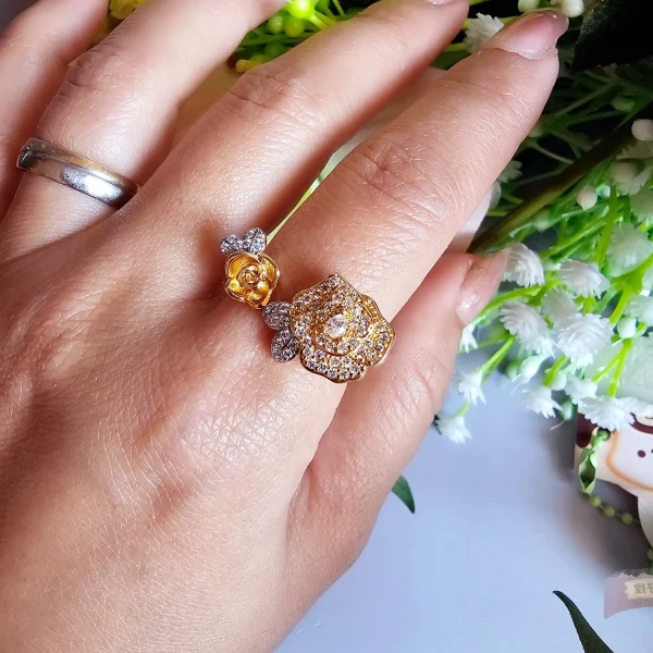 Luxuriöse Damenring mit Kristallbesatz – Filigranes Doppel-Blüten Design Der Damenring zeigt zwei stilisierte Rosenblüten: Eine Blüte ist glatt und poliert, die andere ist dicht mit kleinen, funkelnden Kristallen (Pavé-Optik) besetzt und hat einen größeren Kristall in der Mitte. Der Ring getragen auf den Link Hand mit Blumen Hintergrund.