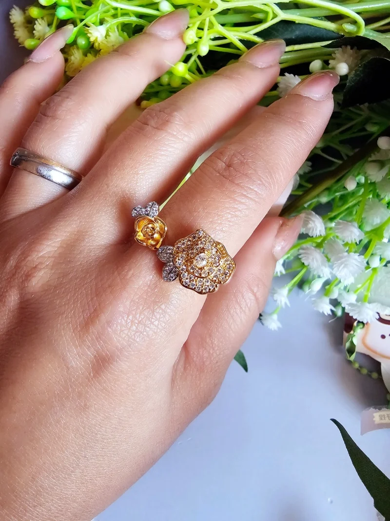 Luxuriöse Damenring mit Kristallbesatz – Filigranes Doppel-Blüten Design Der Damenring zeigt zwei stilisierte Rosenblüten: Eine Blüte ist glatt und poliert, die andere ist dicht mit kleinen, funkelnden Kristallen (Pavé-Optik) besetzt und hat einen größeren Kristall in der Mitte. Der Ring getragen auf den Link Hand mit Blumen Hintergrund.