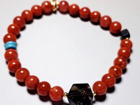 Achat-AB009-05 Elastisches Perlenarmband aus polierten roten Achat-Steinen mit warmem Glanz, veredelt durch goldfarbene Zwischenelemente. Im Mittelpunkt steht ein facettierter, dunkler Mittelanhänger, der dem Design Tiefe und Eleganz verleiht. Dezente Akzentperlen in Türkis und Dunkelblau setzen farbliche Kontraste und runden das Gesamtbild harmonisch ab. Minimalistisch, edel und vielseitig kombinierbar – ideal als stilvolles Accessoire für Alltag und besondere Anlässe oder als Geschenkidee.