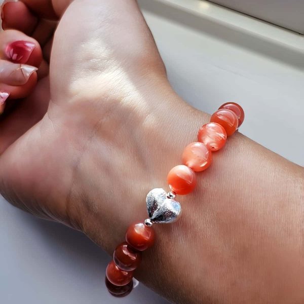 AB-ACT-05 Damenarmband aus rotem Achat Kugeln Bergkristall fein poliert mit versilberten Details und chinesischen Schriftzeichen getragen am Handgelenk bei Sonnenschein.