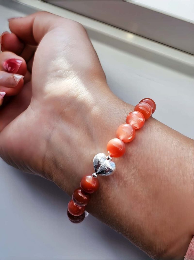 AB-ACT-05 Damenarmband aus rotem Achat Kugeln Bergkristall fein poliert mit versilberten Details und chinesischen Schriftzeichen getragen am Handgelenk bei Sonnenschein.