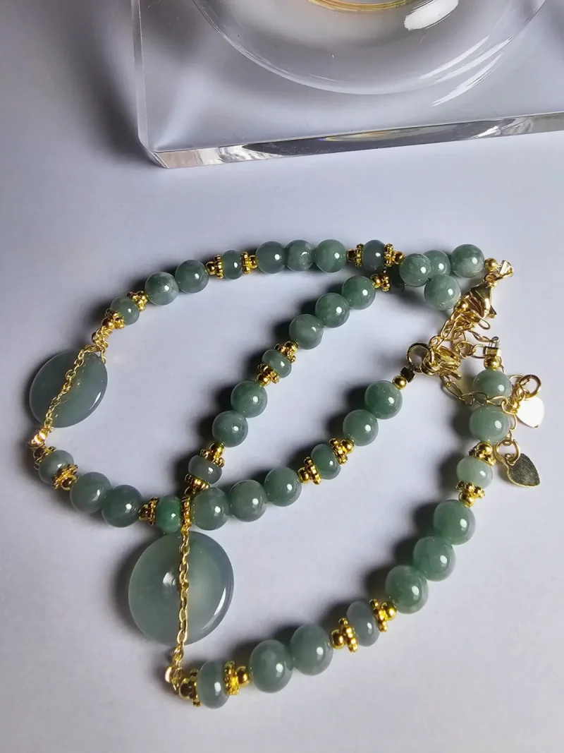 Blauwasser Jade Armband Naturstein Handgefertigtes Jade Armband aus blau-grünen Jade-Perlen mit goldenen Trennperlen und einem runden Jade-Anhänger (Ping-An-Knopf). Eleganter Schmuck mit traditioneller chinesischer Symbolik.