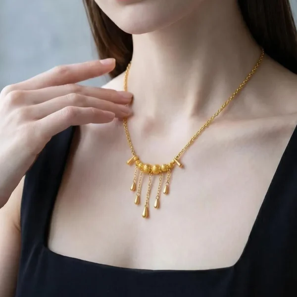 Elegante Goldene Tropfen-Fransen Halskette – Vintage Laser-Design mit schimmernden Kugeln Porträt einer Junge Frau mit dunkle Schwarz Hair. Sie trägt eine Schwarz U-schnitt T-Shirt und eine filigrane, goldfarbene Halskette. Der Anhänger der Kette besteht aus einer horizontalen Reihe kleiner, glänzender Kugeln, von denen mehrere feine Kettchen mit Tropfen-Formen herabhängen (Vintage-Fransen-Design).