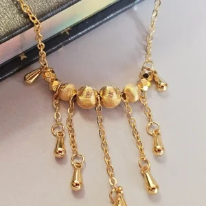 Goldfarbene Modeschmuck-Halskette aus Kupfer, bestehend aus einer feinen Kette und einem mittigen Anhänger mit drei geriffelten Laser-Kugeln, von denen fünf filigrane Ketten mit kleinen Tropfen-Anhängern herabfallen.