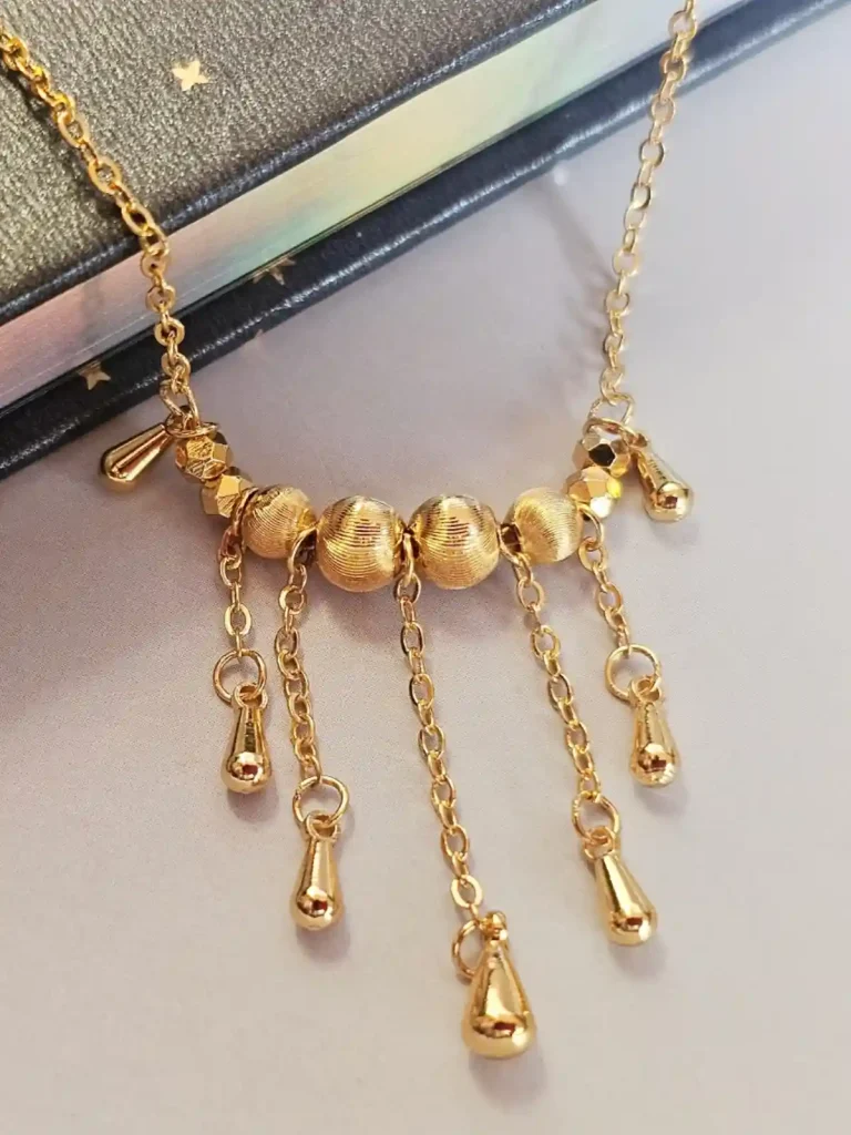 Halskette mit goldenen Tropfen und schimmernden Kugeln - Vintage Stil Goldfarbene Modeschmuck-Halskette aus Kupfer, bestehend aus einer feinen Kette und einem mittigen Anhänger mit drei geriffelten Laser-Kugeln, von denen fünf filigrane Ketten mit kleinen Tropfen-Anhängern herabfallen.