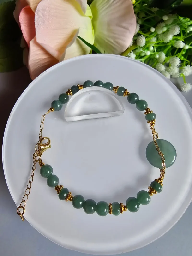 Blauwasser Jade Armband Naturstein Handgefertigtes Jade Armband aus blau-grünen Jade-Perlen mit goldenen Trennperlen und einem runden Jade-Anhänger (Ping-An-Knopf). Eleganter Schmuck mit traditioneller chinesischer Symbolik.