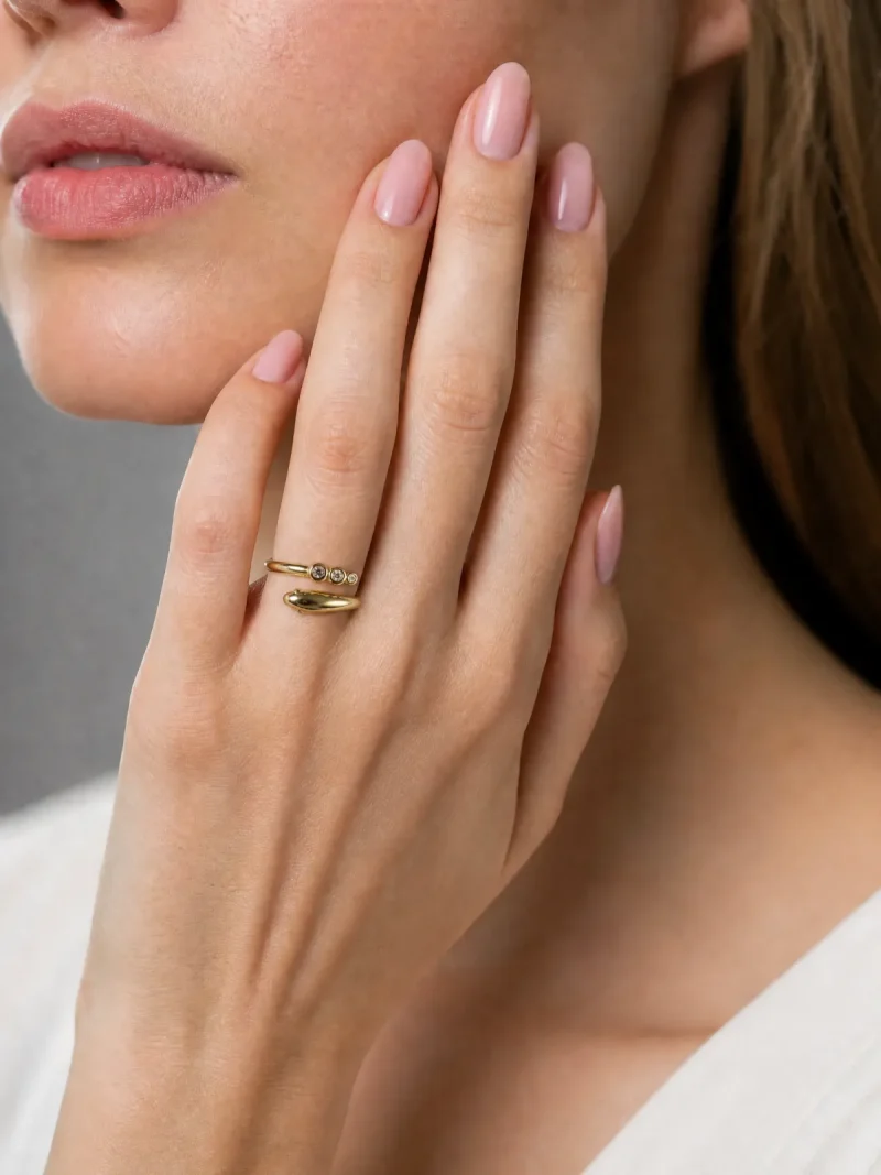 Nahaufnahme einer Frauenhand mit einem goldenen Schlangenring, der mit drei kleinen Zirkonia-Steinen besetzt ist. Der Ring wird elegant am Kinn präsentiert.