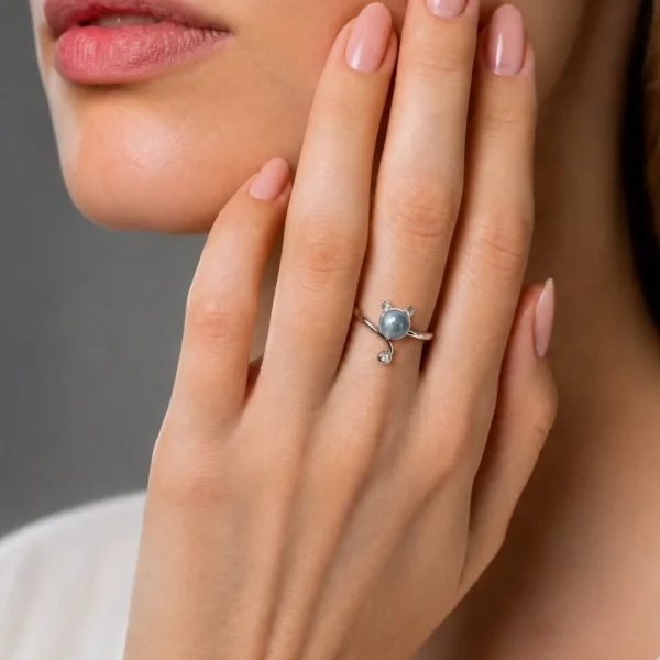 Mondstein Ring Katze Design – offener verstellbarer Damenring mit Zirkonia Nahaufnahme einer Frauenhand mit einem silbernen Ring in Katzenform, der einen grauen Edelstein als Kopf und kleine Ohren aufweist. Der Ring wird elegant vor dem Gesicht der Frau präsentiert.