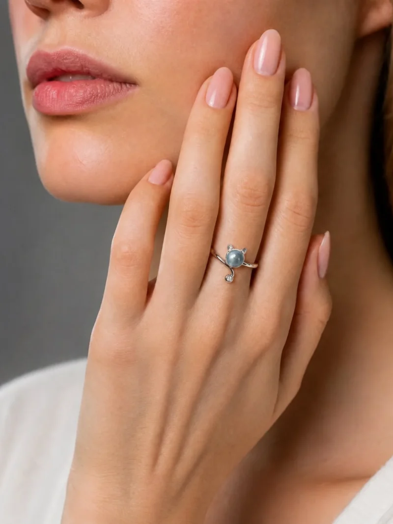 Mondstein Ring Katze Design – offener verstellbarer Damenring mit Zirkonia Nahaufnahme einer Frauenhand mit einem silbernen Ring in Katzenform, der einen grauen Edelstein als Kopf und kleine Ohren aufweist. Der Ring wird elegant vor dem Gesicht der Frau präsentiert.