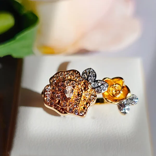 Luxuriöse Halskette und Damenring Set mit Kristallbesatz – Filigranes Doppel-Blüten Design Nahaufnahme einer goldfarbenen Damenring. Der Set zeigt zwei stilisierte Rosenblüten: Eine Blüte ist glatt und poliert, die andere ist dicht mit kleinen, funkelnden Kristallen (Pavé-Optik) besetzt und hat einen größeren Kristall in der Mitte.