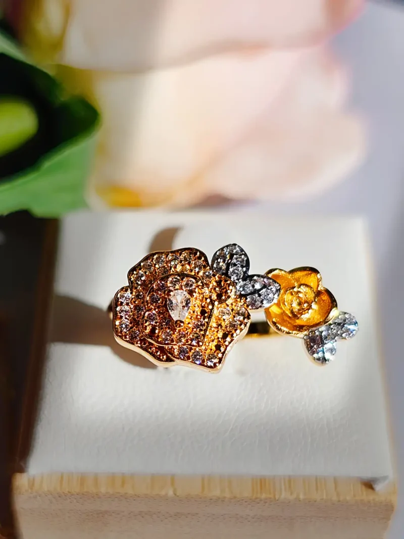 Luxuriöse Halskette und Damenring Set mit Kristallbesatz – Filigranes Doppel-Blüten Design Nahaufnahme einer goldfarbenen Damenring. Der Set zeigt zwei stilisierte Rosenblüten: Eine Blüte ist glatt und poliert, die andere ist dicht mit kleinen, funkelnden Kristallen (Pavé-Optik) besetzt und hat einen größeren Kristall in der Mitte.