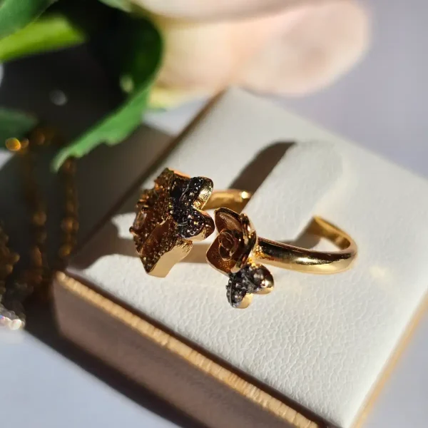 Luxuriöse Halskette und Damenring Set mit Kristallbesatz – Filigranes Doppel-Blüten Design Nahaufnahme einer goldfarbenen Damenring. Der Set zeigt zwei stilisierte Rosenblüten: Eine Blüte ist glatt und poliert, die andere ist dicht mit kleinen, funkelnden Kristallen (Pavé-Optik) besetzt und hat einen größeren Kristall in der Mitte.