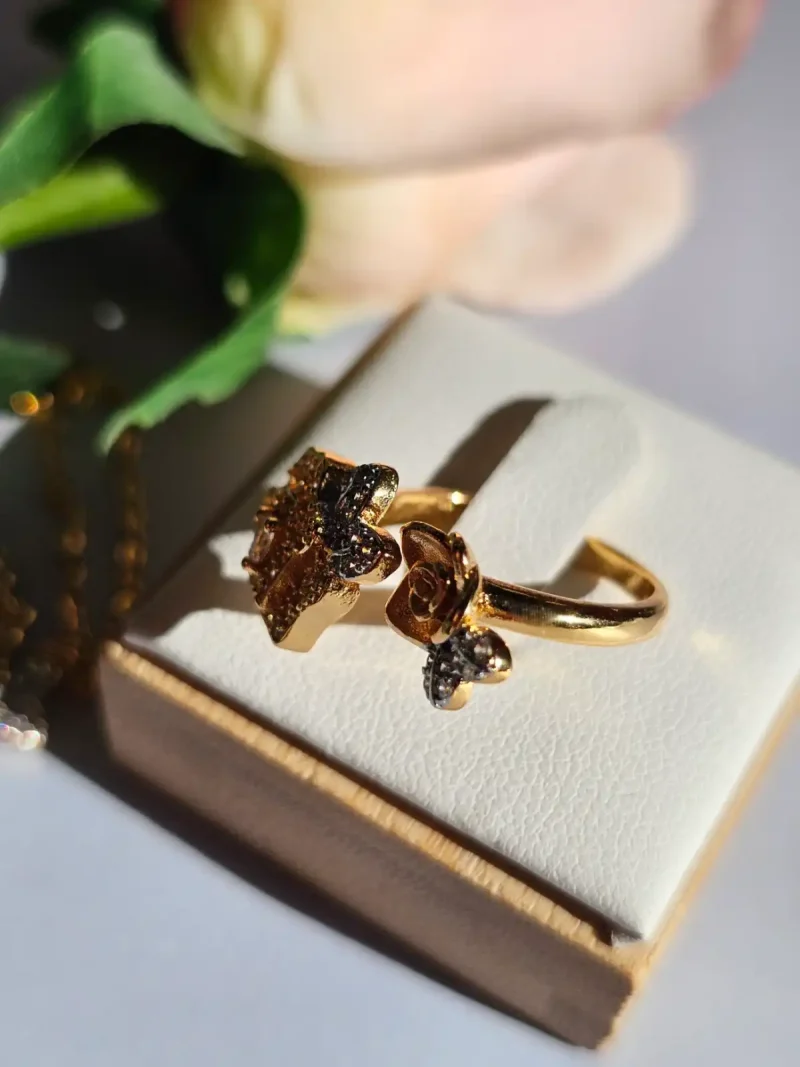 Luxuriöse Halskette und Damenring Set mit Kristallbesatz – Filigranes Doppel-Blüten Design Nahaufnahme einer goldfarbenen Damenring. Der Set zeigt zwei stilisierte Rosenblüten: Eine Blüte ist glatt und poliert, die andere ist dicht mit kleinen, funkelnden Kristallen (Pavé-Optik) besetzt und hat einen größeren Kristall in der Mitte.