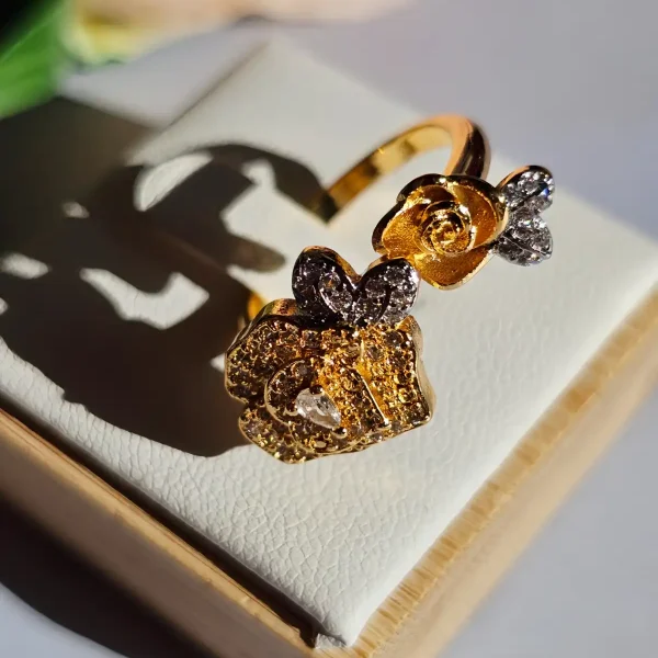Luxuriöse Halskette und Damenring Set mit Kristallbesatz – Filigranes Doppel-Blüten Design Nahaufnahme einer goldfarbenen Damenring. Der Set zeigt zwei stilisierte Rosenblüten: Eine Blüte ist glatt und poliert, die andere ist dicht mit kleinen, funkelnden Kristallen (Pavé-Optik) besetzt und hat einen größeren Kristall in der Mitte.