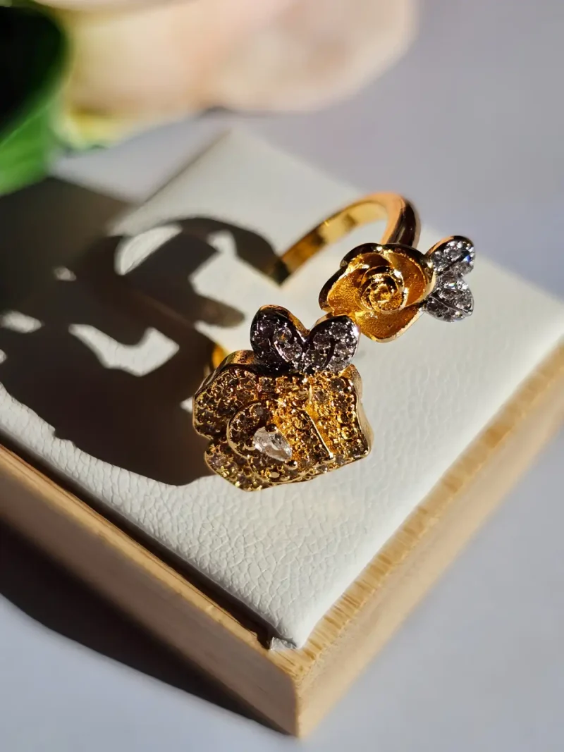 Luxuriöse Halskette und Damenring Set mit Kristallbesatz – Filigranes Doppel-Blüten Design Nahaufnahme einer goldfarbenen Damenring. Der Set zeigt zwei stilisierte Rosenblüten: Eine Blüte ist glatt und poliert, die andere ist dicht mit kleinen, funkelnden Kristallen (Pavé-Optik) besetzt und hat einen größeren Kristall in der Mitte.