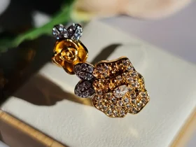 Luxuriöse Halskette und Damenring Set mit Kristallbesatz – Filigranes Doppel-Blüten Design Nahaufnahme einer goldfarbenen Damenring. Der Set zeigt zwei stilisierte Rosenblüten: Eine Blüte ist glatt und poliert, die andere ist dicht mit kleinen, funkelnden Kristallen (Pavé-Optik) besetzt und hat einen größeren Kristall in der Mitte.