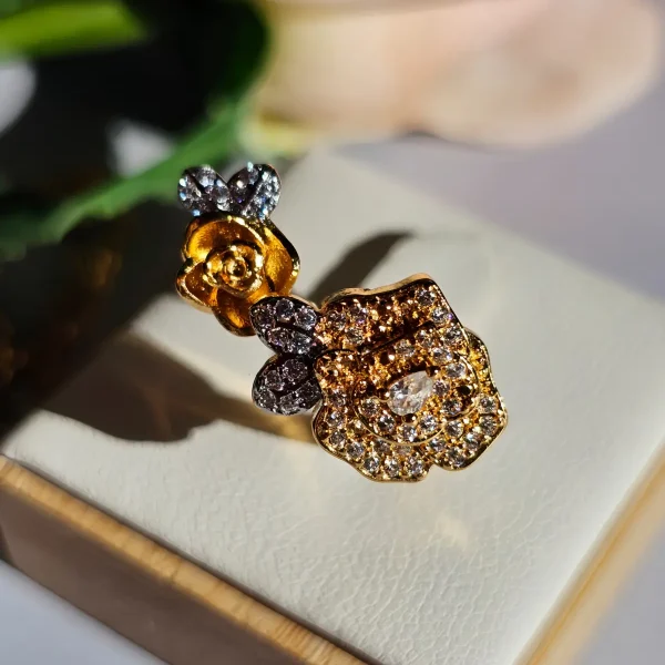 Luxuriöse Halskette und Damenring Set mit Kristallbesatz – Filigranes Doppel-Blüten Design Nahaufnahme einer goldfarbenen Damenring. Der Set zeigt zwei stilisierte Rosenblüten: Eine Blüte ist glatt und poliert, die andere ist dicht mit kleinen, funkelnden Kristallen (Pavé-Optik) besetzt und hat einen größeren Kristall in der Mitte.