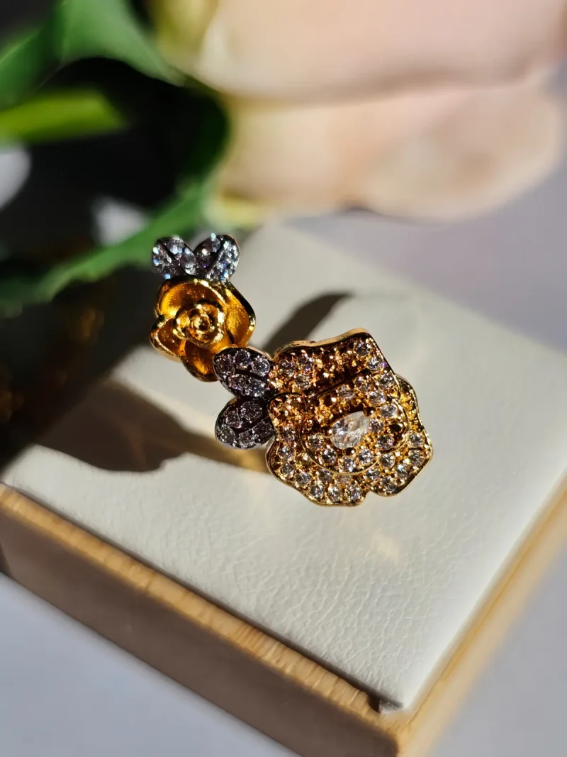 Luxuriöse Halskette und Damenring Set mit Kristallbesatz – Filigranes Doppel-Blüten Design Nahaufnahme einer goldfarbenen Damenring. Der Set zeigt zwei stilisierte Rosenblüten: Eine Blüte ist glatt und poliert, die andere ist dicht mit kleinen, funkelnden Kristallen (Pavé-Optik) besetzt und hat einen größeren Kristall in der Mitte.
