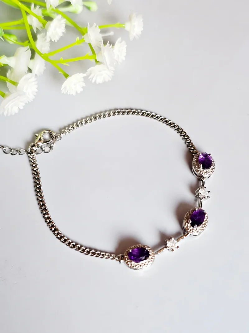 Amethyst Armband aus Kupfer versilbert Amethyst Armband aus silberfarbenem Metall mit ovalen violetten Steinen und funkelnden Zirkonia-Details auf lichtblau Hintergrund mit Blumen