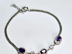 Amethyst Armband aus silberfarbenem Metall mit ovalen violetten Steinen und funkelnden Zirkonia-Details auf lichtblau Hintergrund mit Blumen