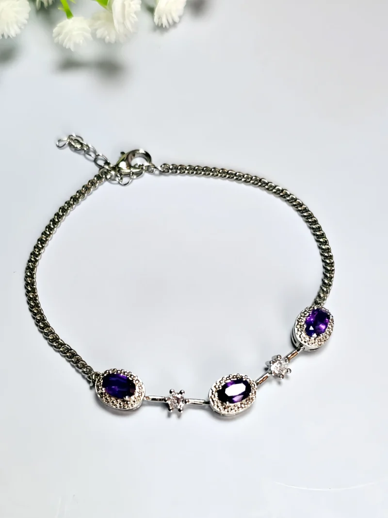 Amethyst Armband aus Kupfer versilbert Amethyst Armband aus silberfarbenem Metall mit ovalen violetten Steinen und funkelnden Zirkonia-Details auf lichtblau Hintergrund mit Blumen