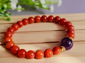 Achat-AB04-01 ein rotes Damenarmband mit Roter Achat Naturstein und violetter Lepidolith-Zentralperle auf einem Holzplatte, vor einer Blumenhintergrund