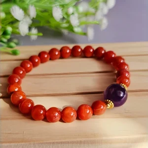 ein rotes Damenarmband mit Roter Achat Naturstein und violetter Lepidolith-Zentralperle auf einem Holzplatte, vor einer Blumenhintergrund