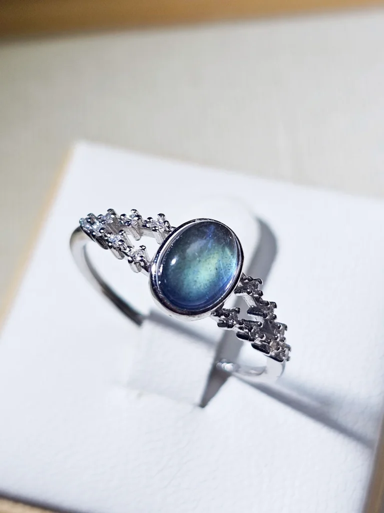 Silberring mit ovalem, blau schimmerndem Mondstein und filigraner Ringschiene, verziert mit funkelnden Zirkonia-Steinen.