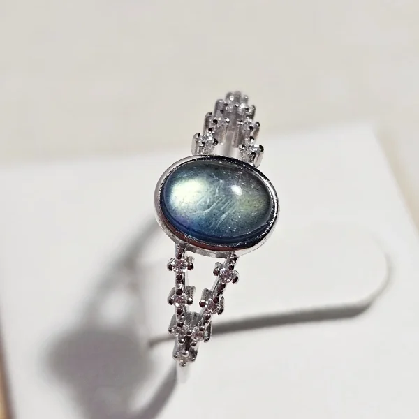 DR-SIL-03-02 Silberring mit ovalem, blau schimmerndem Mondstein und filigraner Ringschiene, verziert mit funkelnden Zirkonia-Steinen.