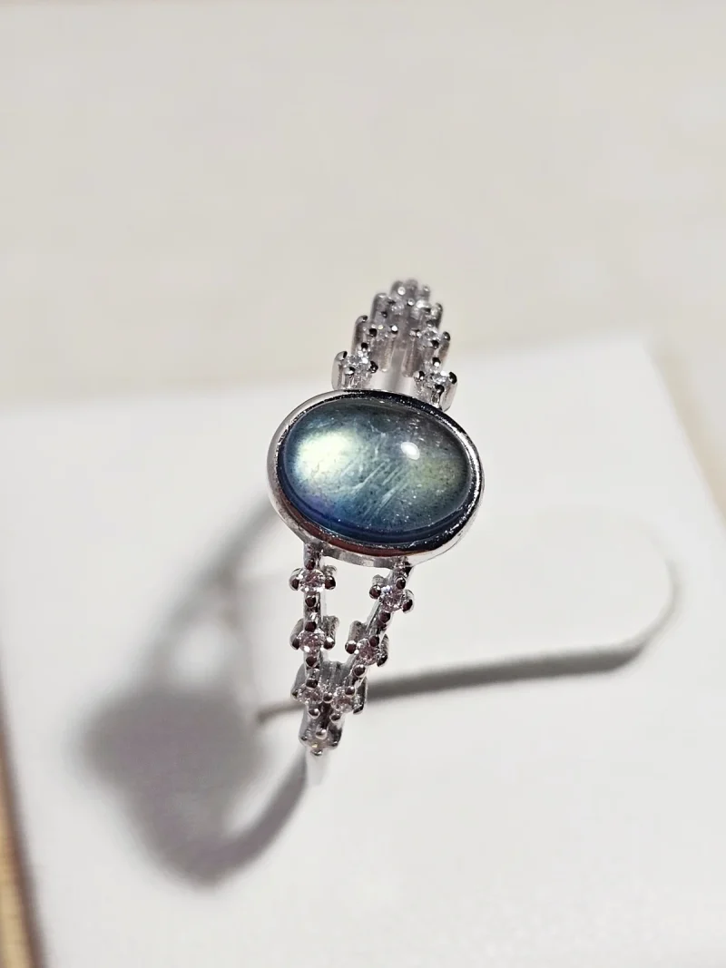 DR-SIL-03-02 Silberring mit ovalem, blau schimmerndem Mondstein und filigraner Ringschiene, verziert mit funkelnden Zirkonia-Steinen.