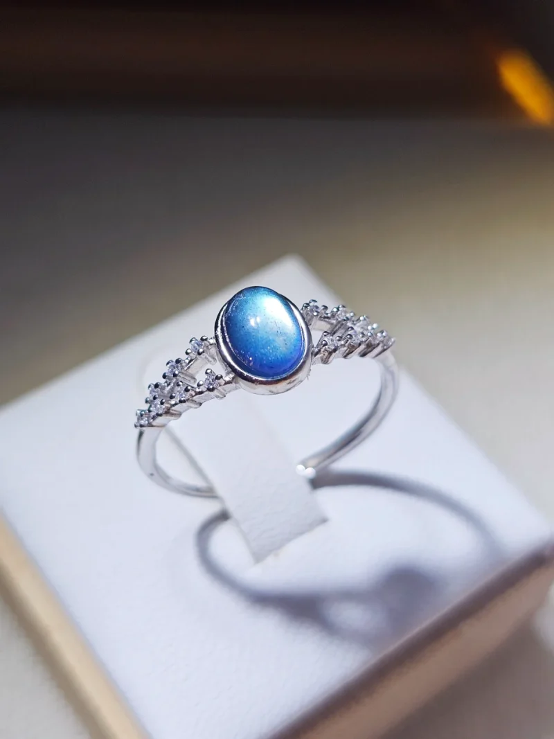 DR-SIL-03-03 Silberring mit ovalem, blau schimmerndem Mondstein und filigraner Ringschiene, verziert mit funkelnden Zirkonia-Steinen.